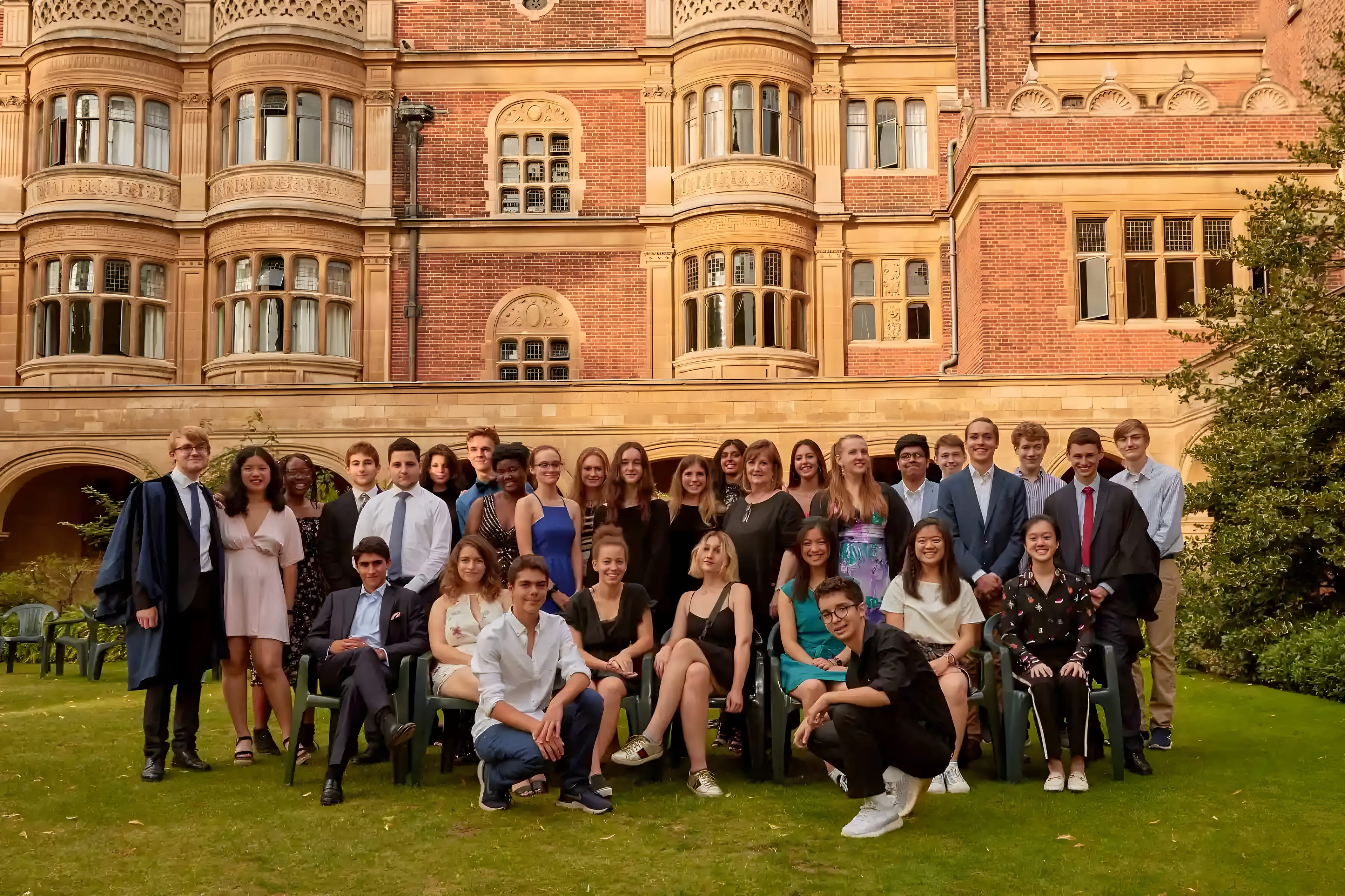 A group of students posed together on a lawn in front of a red-brick building