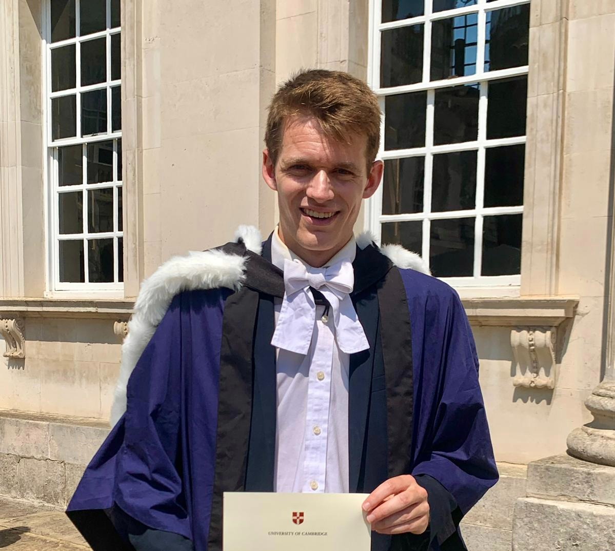 A graduate in academic gown holding a certificate
