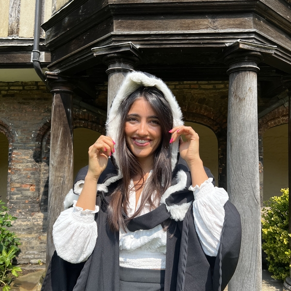 A graduate in academic gown and hood outside a college